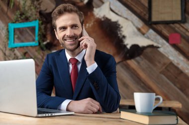 Genç işadamı gülümsüyor ve telefonda konuşuyor, kahve dükkanında çalışmak istiyor.