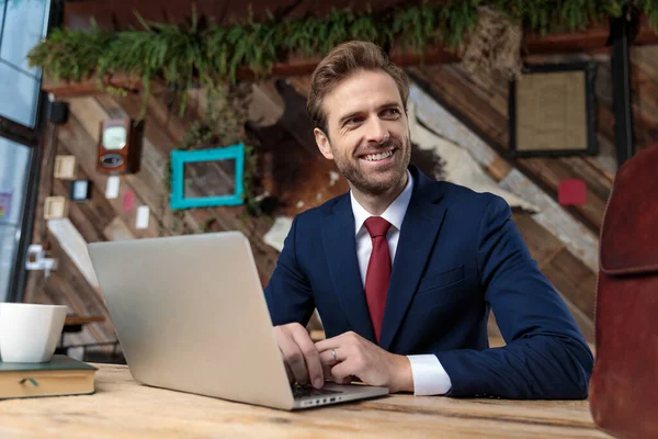 穿着西服的年轻商人在笔记本电脑上工作 面带微笑地坐在咖啡店里 — 图库照片