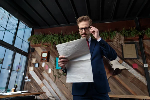 スーツ姿の若いビジネスマンがニュースを読み眼鏡を調整しコーヒーショップに立ち — ストック写真