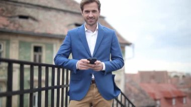 Parmaklıkların üzerinde dinlenen denizci kıyafeti giyen yakışıklı bir işadamı. Sonra da dışarıda merdivenlerin yanında mutlu bir şekilde iki parmakla selam veriyor.