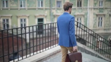 Şehrin dışında bir evrak çantasını tutarken merdivenlerden inen çekici bir işadamının arka görüntüsü.