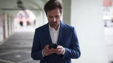 Donanma kıyafeti giyen seksi iş adamı telefonuna mesaj yazıyor ve şehrin dışında mutlu bir şekilde kameraya bakıyor.