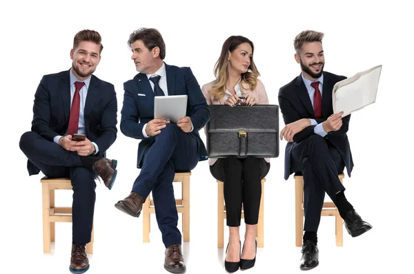 由4名商人组成的小组在等待求职面试时手持电话 报纸和公文包 坐在有白色工作室背景的椅子上 — 图库照片