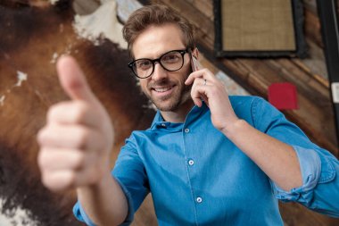 Pozitif model onaylıyor, telefonda konuşuyor mavi gömlek ve gözlük takıyor, kahve falı üzerinde bir masada oturuyor.