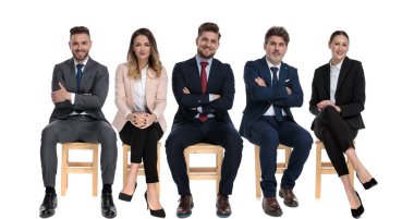 5 pozitif iş adamından oluşan bir ekip iş görüşmesini beklerken gülümsüyor ve beyaz stüdyo arka planında sandalyelerde oturuyor.