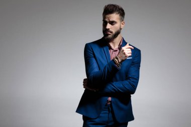 Seksi iş adamı kollarını kavuşturup gri stüdyo arka planında havalı bir tavırla dikiliyor.