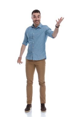 Mavi gömlek giyerken gülümseyen ve açıklama yapan, beyaz stüdyo arka planında duran,