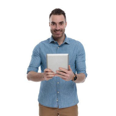 Mavi gömlek giyerken elinde tablet tutan ve gülümseyen mutlu bir adam, beyaz stüdyo arka planında duruyor.