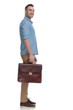 Mavi gömlek giyip, beyaz stüdyo arka planında dururken gülümseme ve evrak çantası taşımanın yan görüntüsü.