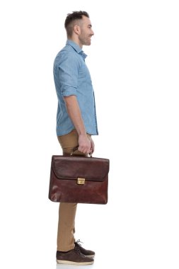 Mavi gömlek giyerken ve beyaz stüdyo arka planında dururken güler yüzlü ve evrak çantası tutan kendine güvenen insanların yan görüntüsü.