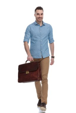 Mavi gömlek giyerken gülümseyen ve evrak çantası tutan, beyaz stüdyo arka planında yürüyen sıradan bir adam.