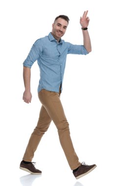 Mavi gömlek giyerken gülümseyen ve selamlaşan, beyaz stüdyo arka planına basan...