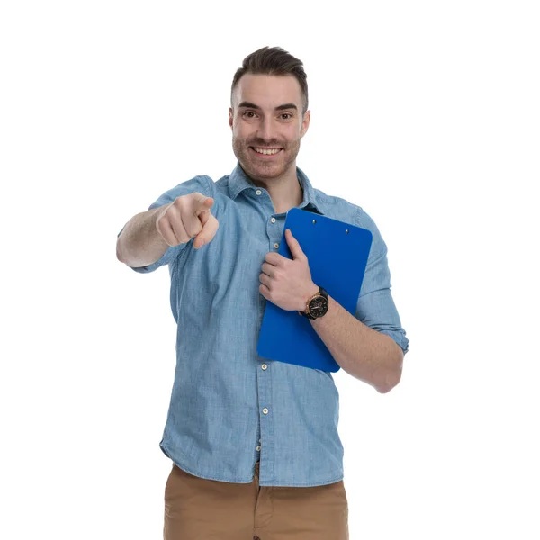 Hombre Casual Guapo Sosteniendo Portapapeles Apuntando Hacia Adelante Sonriendo Mientras —  Fotos de Stock