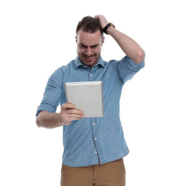 身穿蓝色衬衫 手举着手看着平板电脑 站在白色工作室的背景下哭泣 — 图库照片