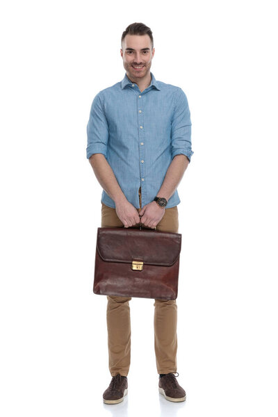 Positive casual man smiling and holding briefcase while wearing blue shirt, standing on white studio background