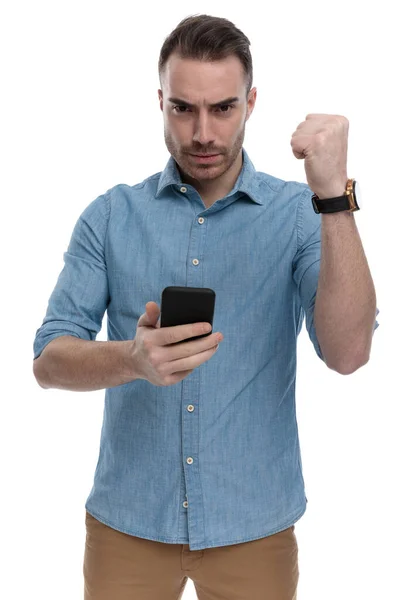 Zdenerwowany Nieformalny Mężczyzna Trzymający Telefon Marszczący Brwi Pięścią Zaciśnięty Podczas — Zdjęcie stockowe