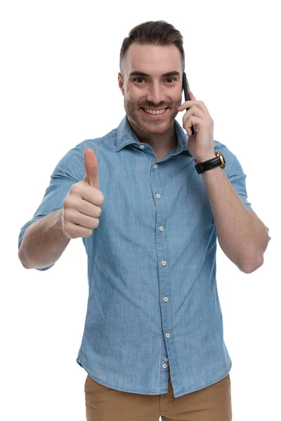 快乐而随意的男人 穿着蓝色衬衫 站在白色的工作室背景上 一边打电话 一边笑 一边摆姿势 — 图库照片