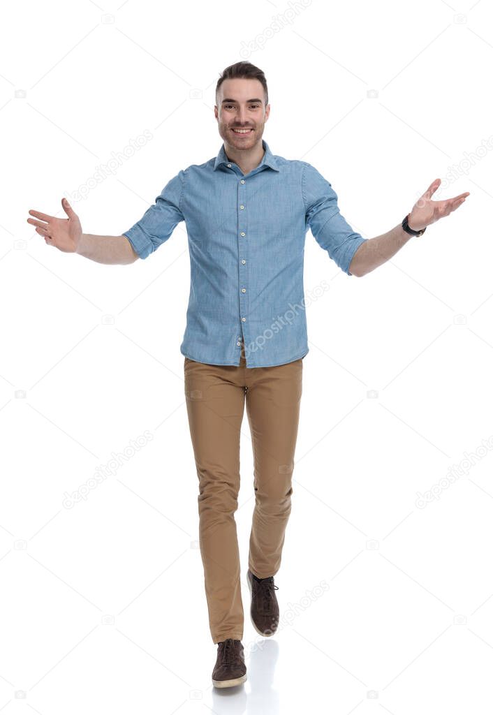 Cheerful casual man smiling and welcoming while wearing blue shirt, stepping on white studio background