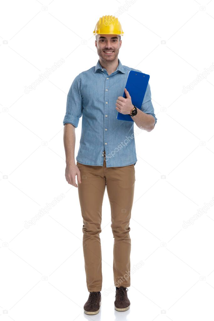 Happy casual man wearing construction helmet and holding clipboard, standing on white studio background