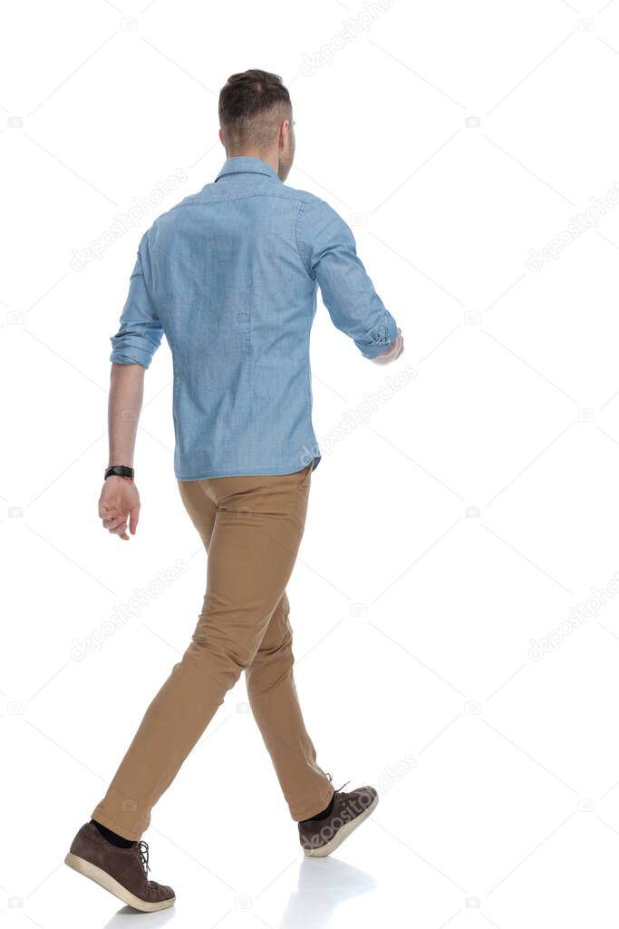 Rear view of casual man walking while wearing blue shirt on white studio background