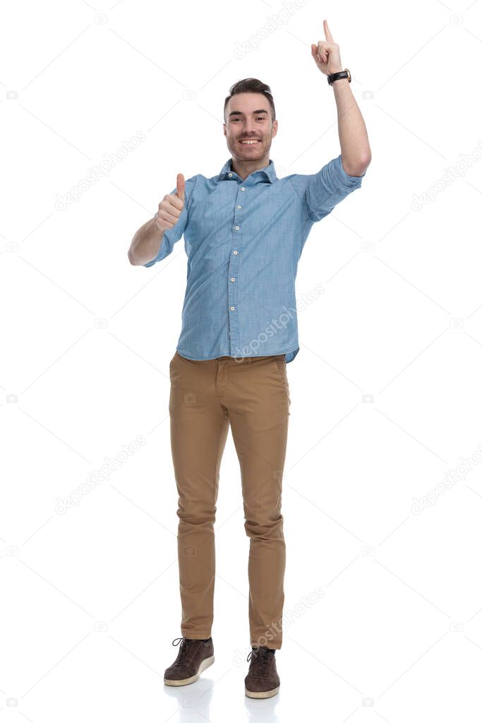 Positive casual man pointing up and gesturing ok while wearing blue shirt, standing on white studio background