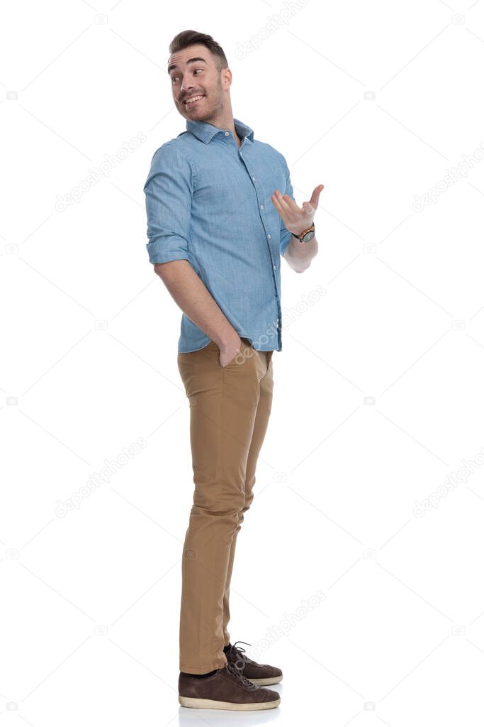 Side view of cheerful casual man laughing and explaining while wearing blue shirt, standing on white studio background