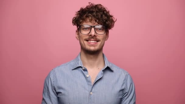 眼鏡をかけた魅力的なカジュアルな男が立って笑顔で幸せならピンクのスタジオの背景に両手で親指をあげる — ストック動画