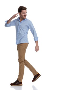 Beyaz stüdyo arka planında yürürken gülümseyen ve selamlaşan mutlu sıradan bir adamın yan görüntüsü