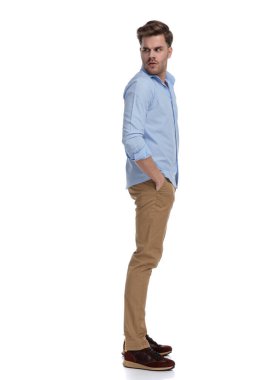 Gömlek giyerken ve beyaz stüdyo arka planında dururken elleri ceplerinde omzunun üstünden bakan sıradan bir adamın yan görüntüsü.