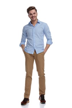 Gömlek giyerken elleri ceplerinde gülümseyen ve beyaz stüdyo arka planında duran sıradan bir adam.