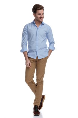 Yakışıklı, sıradan bir adam gömlek giyerken ve beyaz stüdyo arka planında dururken elini cebine atarak gülümsüyor.