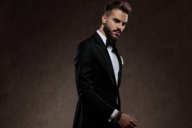 Sıkıntılı moda damadı takım elbise giyerken kaşlarını çatıyor ve ileriye bakıyor, duvar kağıdı stüdyosunda yürüyor.