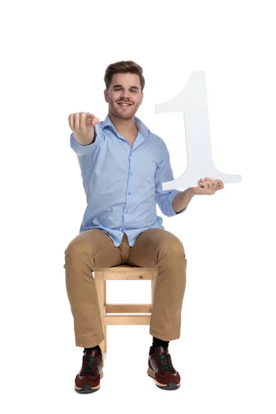 快乐而随意的男人拿着第一棒 微笑着指指点点 坐在白色摄影棚的椅子上 — 图库照片