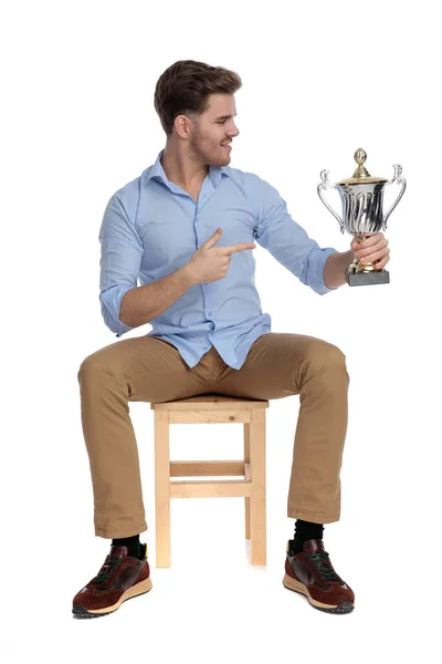 Orgulhoso Homem Casual Segurando Troféu Apontando Para Ele Enquanto Sentado — Fotografia de Stock