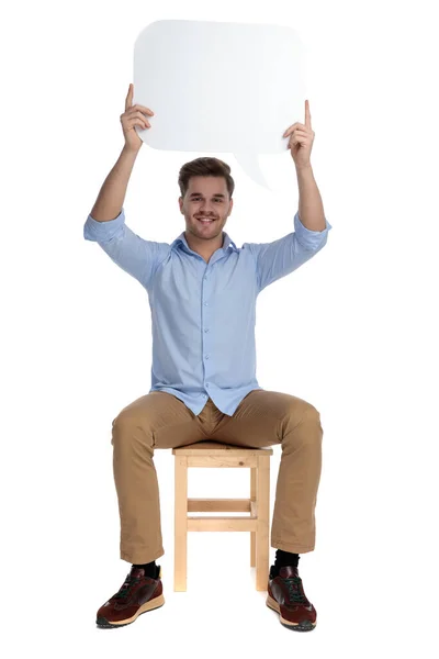 快乐而随意的男人 头顶高耸着话筒 坐在白色工作室背景的椅子上 面带微笑 — 图库照片