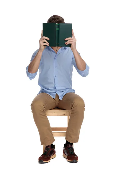 Joven Hombre Casual Cubriendo Cara Con Libro Mientras Está Sentado —  Fotos de Stock