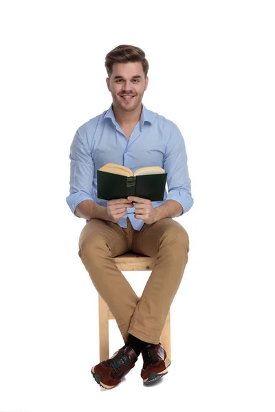 坐在白色工作室背景的椅子上 积极随意的男人一边看书 一边笑着 — 图库照片