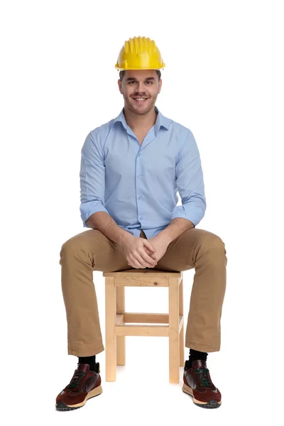 坐在白色工作室背景的椅子上 戴着硬礼帽 面带微笑的快乐而随意的男人 — 图库照片