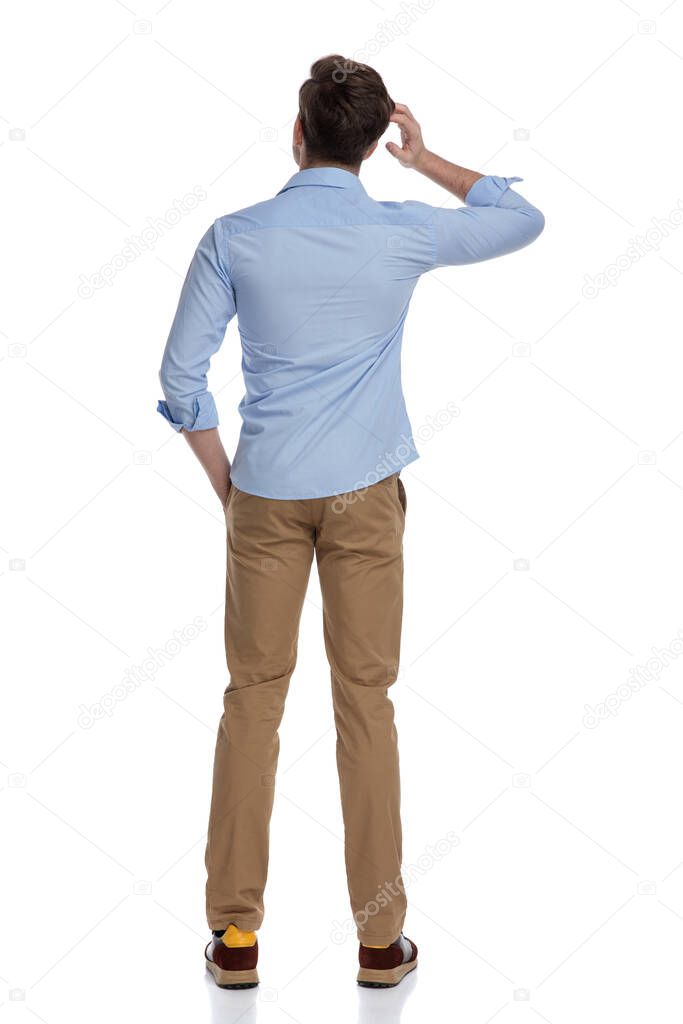 Rear view of confused casual man scratching his head while wearing shirt and standing on white studio background