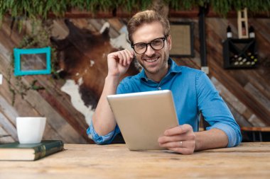 Gözlüklü sıradan bir adam masada oturup tabletini tutarken kahve dükkanında mutlu bir şekilde kameraya bakıyordu.