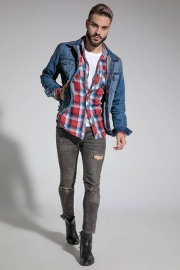 Bir eli cebinde yürüyen ve gri stüdyo arka planında havalı bir tavır sergileyen sıradan bir adam.