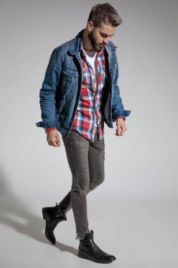 Gri stüdyo arka planında dramatik bir şekilde yürürken kot ceket giyen çekici bir adamın yan görüntüsü.