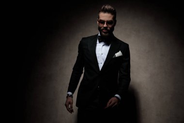 Güneş gözlüğü takan çekici bir iş adamı karanlık stüdyo arka planında kameraya ciddi ciddi bakıyor.