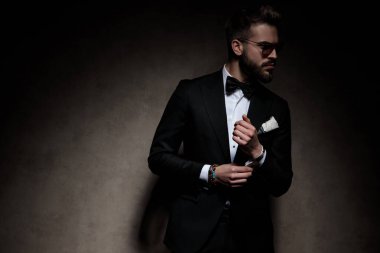 Güneş gözlüğü takan genç bir işadamı karanlık stüdyo geçmişine bakarken kollarını düzeltiyor.