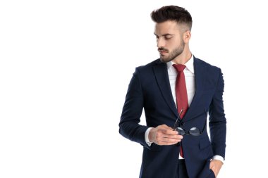 Çekici bir iş adamı, bir eli cepte, diğeriyle gözlük takıyor ve beyaz stüdyo geçmişine tepeden bakıyor.