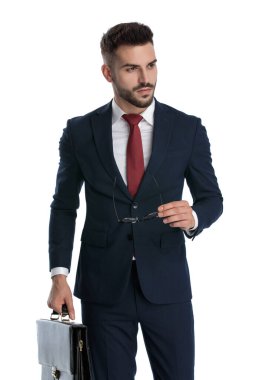 Gözlüklerini çıkarıp beyaz stüdyo geçmişine bakarken elinde evrak çantası tutan seksi bir işadamı.