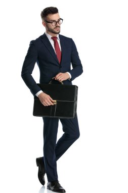 Gözlüklü çekici bir iş adamının yan görünüşü ve beyaz stüdyo arka planında evrak çantasıyla havalı poz vermesi.