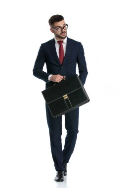 Genç iş adamı gözlüklü, elinde evrak çantasıyla yürüyor ve beyaz stüdyo arka planında havalı bir tavırla başını çeviriyor.