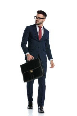 Gözlüklü çekici bir iş adamı elinde evrak çantasıyla dolaşıyor ve beyaz stüdyo geçmişine sert bakıyor.