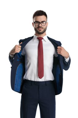 Çekici iş adamı gözlük takıyor ve ceketini çekiyor. Beyaz stüdyo geçmişine sert bakıyor.